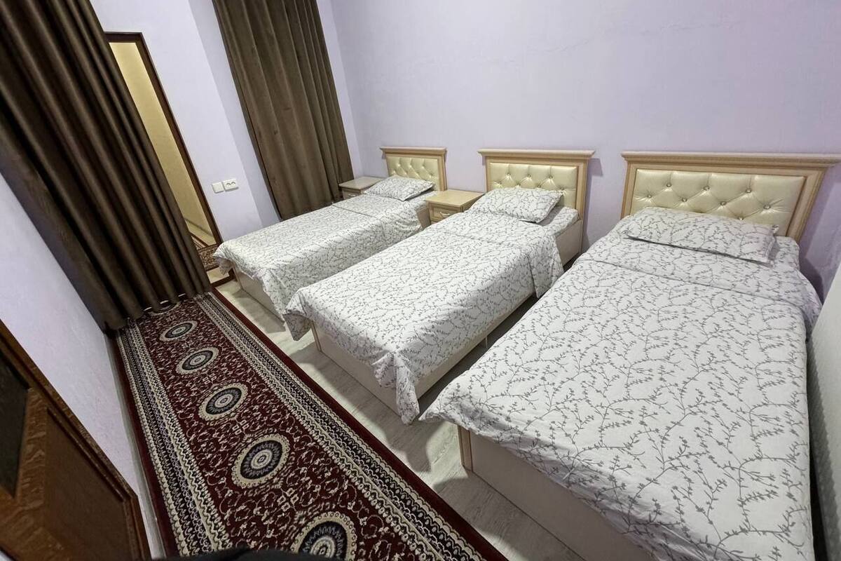 A room with three beds, a patterned carpet, and a curtain.