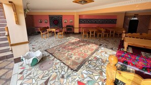 Ein Zimmer mit einem gemusterten Boden, Holzmöbeln, einem dekorativen Teppich und einem Bett mit bunter Decke.