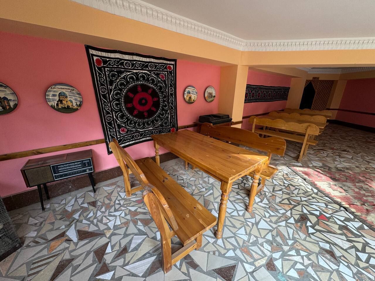 A room with multiple wooden tables and benches, a patterned floor, and decorative wall art.