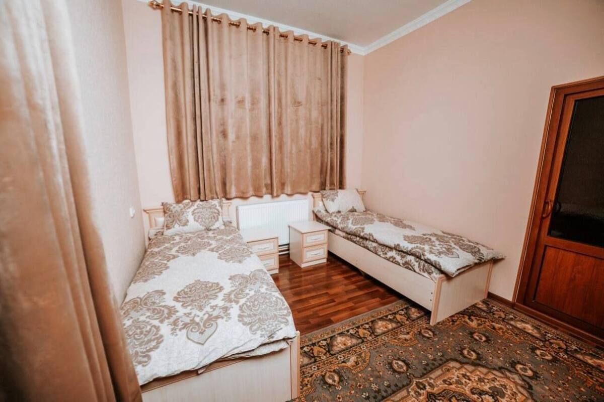 A bedroom with a bed, a bedside table, a small table, a sofa, a patterned rug, and a wooden door.