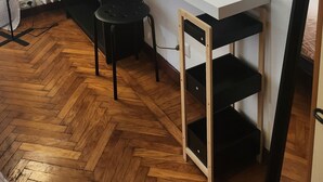 Huoneessa on valkoinen työpöytä, musta tuoli, lattiavalaisin ja patteri.