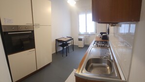 Kompakti keittiö, jossa on sisäänrakennettu uuni, pesuallas sekä ruokailutila, jossa on pöytä ja tuolit.