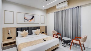 Una camera d'albergo moderna con un letto grande, una scrivania, due poltrone, un condizionatore d'aria e una ventola a soffitto.