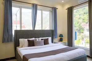 Habitación de hotel con cama, cortinas, mesita de noche y ventana con vistas.