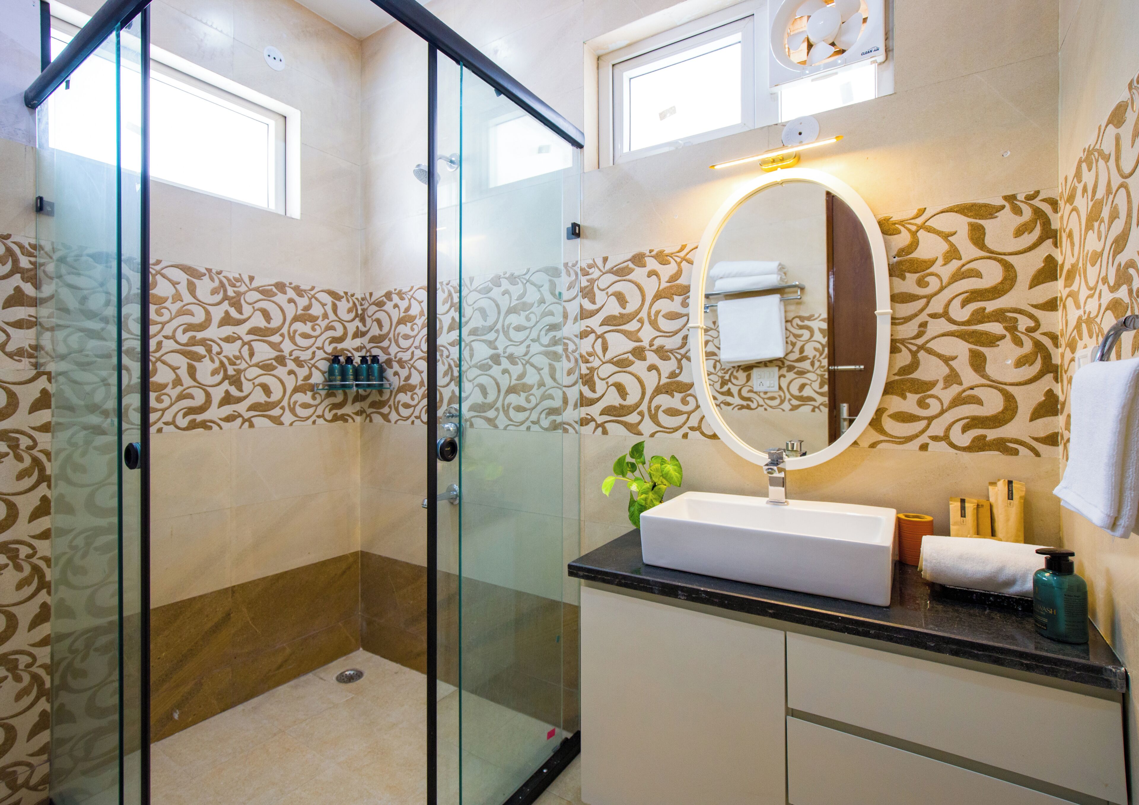 Un baño con ducha de vidrio, lavamanos con espejo y paredes con diseño.