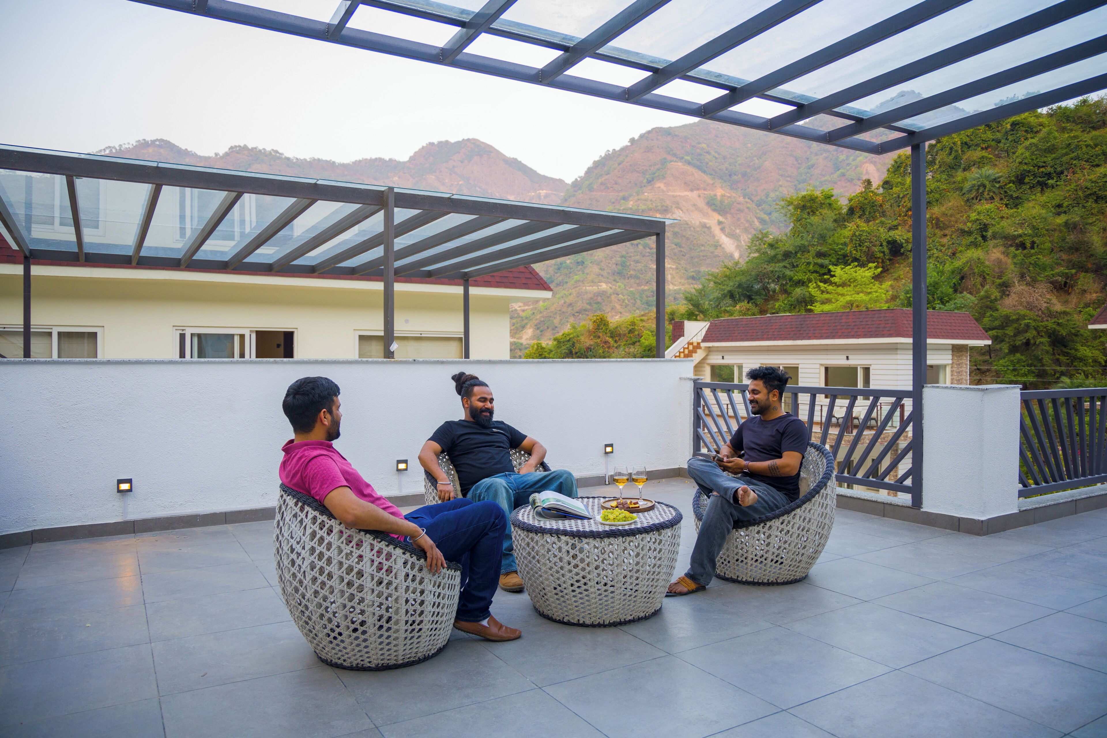 Una terraza en la azotea con tres sillas redondas de mimbre, techo de cristal y montañas al fondo.