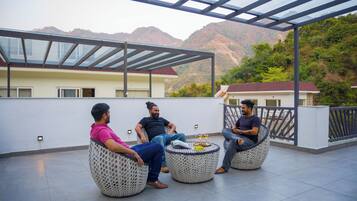 Una terraza en la azotea con tres sillas redondas de mimbre, techo de cristal y montañas al fondo.