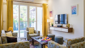 A living room with floral-patterned sofas, a coffee table with snacks, a TV, and a sliding glass door leading to an outdoor area. - ELIVAAS Serenita Abode Tranquil Escape (Bagradhauran)