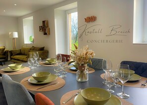 Un coin repas avec une table dressée pour six personnes, un canapé et un mur sur lequel on peut lire l’inscription « Kastell Breizh Conciergerie ».