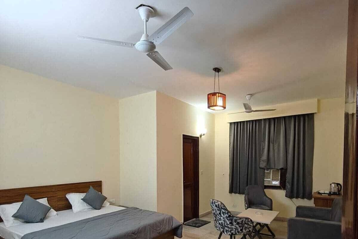 A bedroom with a bed, a chair, a table, a ceiling fan, and a hanging light fixture.
