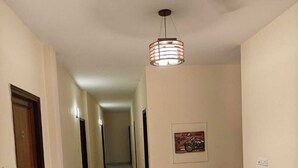 A hallway with a ceiling fan, a framed picture on the wall, and a desk with a chair. - The Grey Leaf Residency (New Delhi)