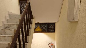 A staircase with marble steps and dark wooden balusters, leading to a landing with a fire extinguisher mounted on the wall. - The Grey Leaf Residency (New Delhi)