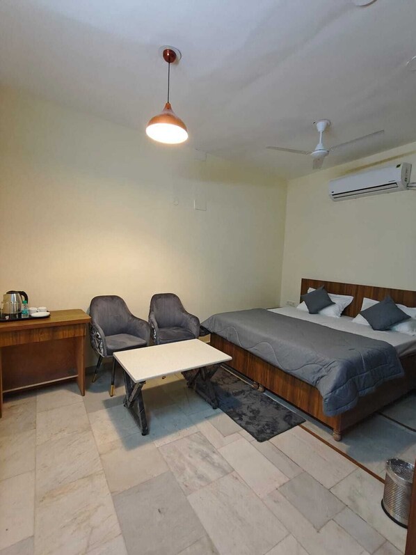 A single bed with a wooden headboard, a desk with a chair, a small table, and a hanging light fixture.