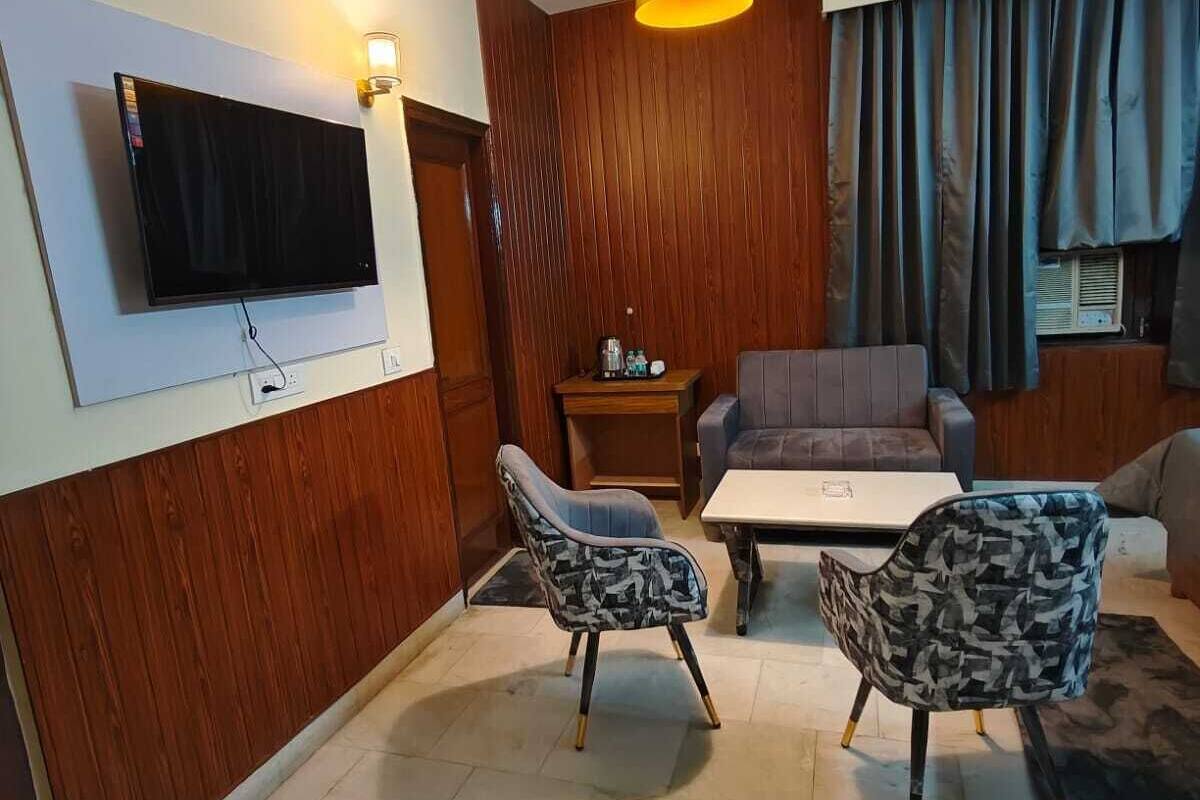 A modern living room with a flat-screen TV, wooden panel walls, a sofa, two patterned chairs, a coffee table, and a hanging pendant light.