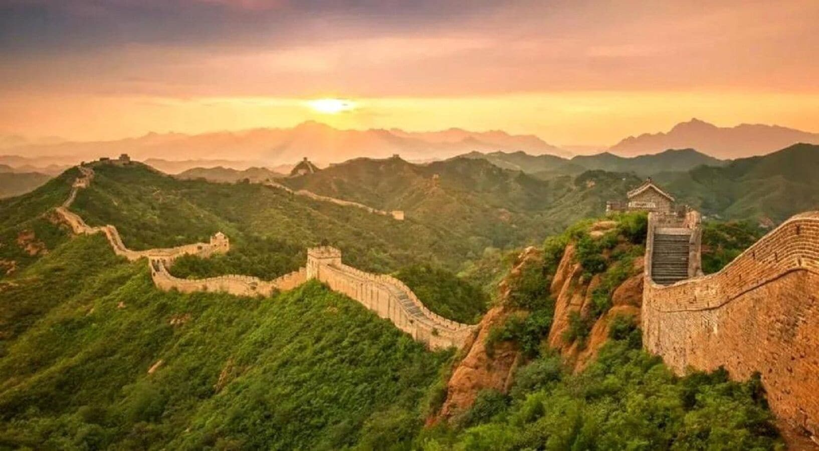 A panoramic view of the Great Wall of China with lush green hills in the background.