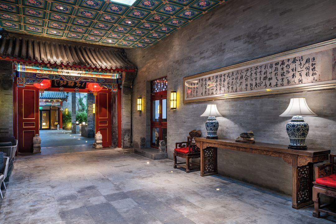 A traditional interior with a tiled floor, a wooden reception desk, and a wall with calligraphy.