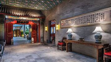 A traditional interior with a tiled floor, a wooden reception desk, and a wall with calligraphy.