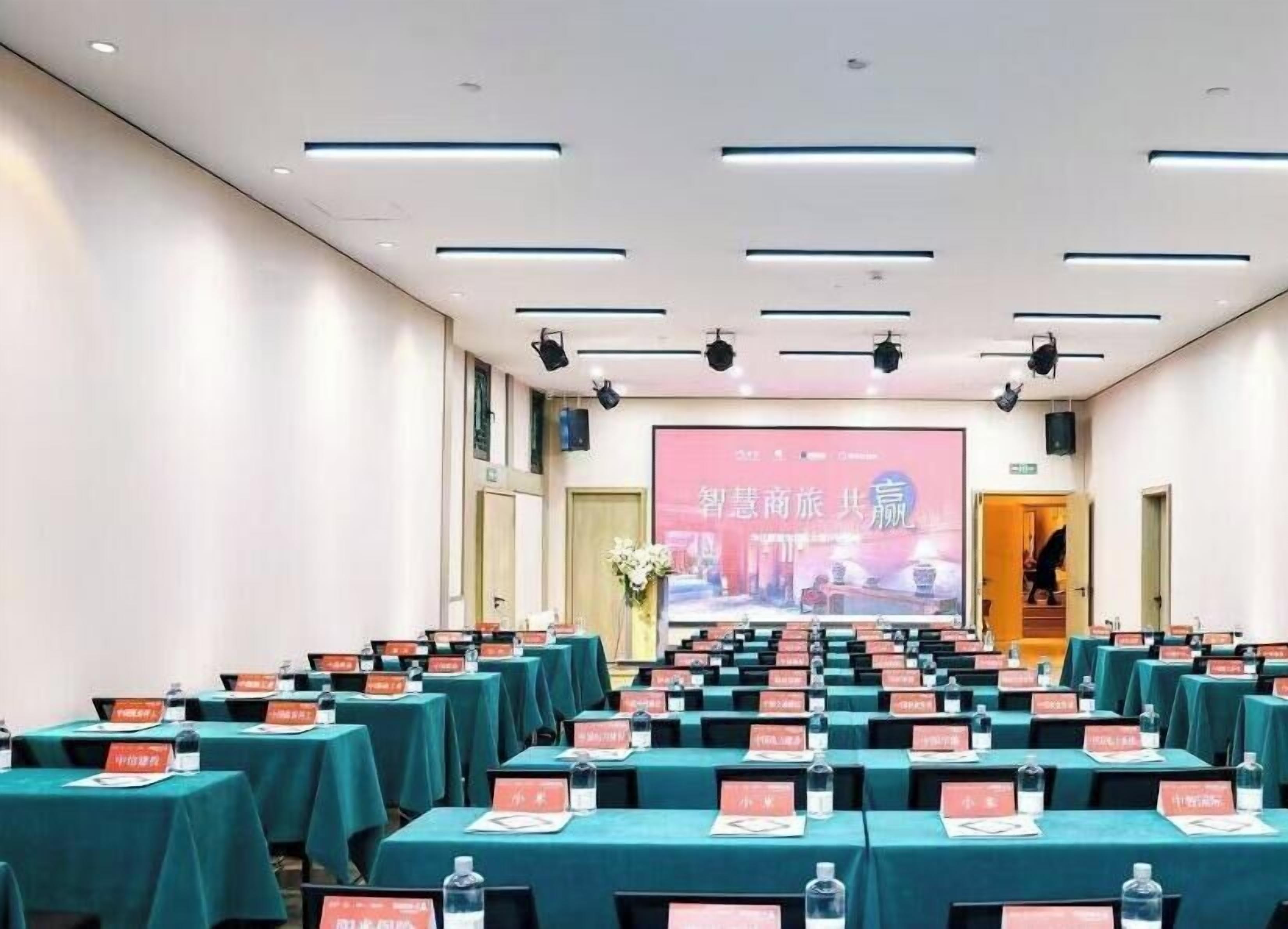 Un salón de conferencias con filas de mesas, tarjetas de identificación y una pantalla grande al frente.