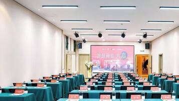 A conference room with rows of tables, nameplates, and a large screen at the front.
