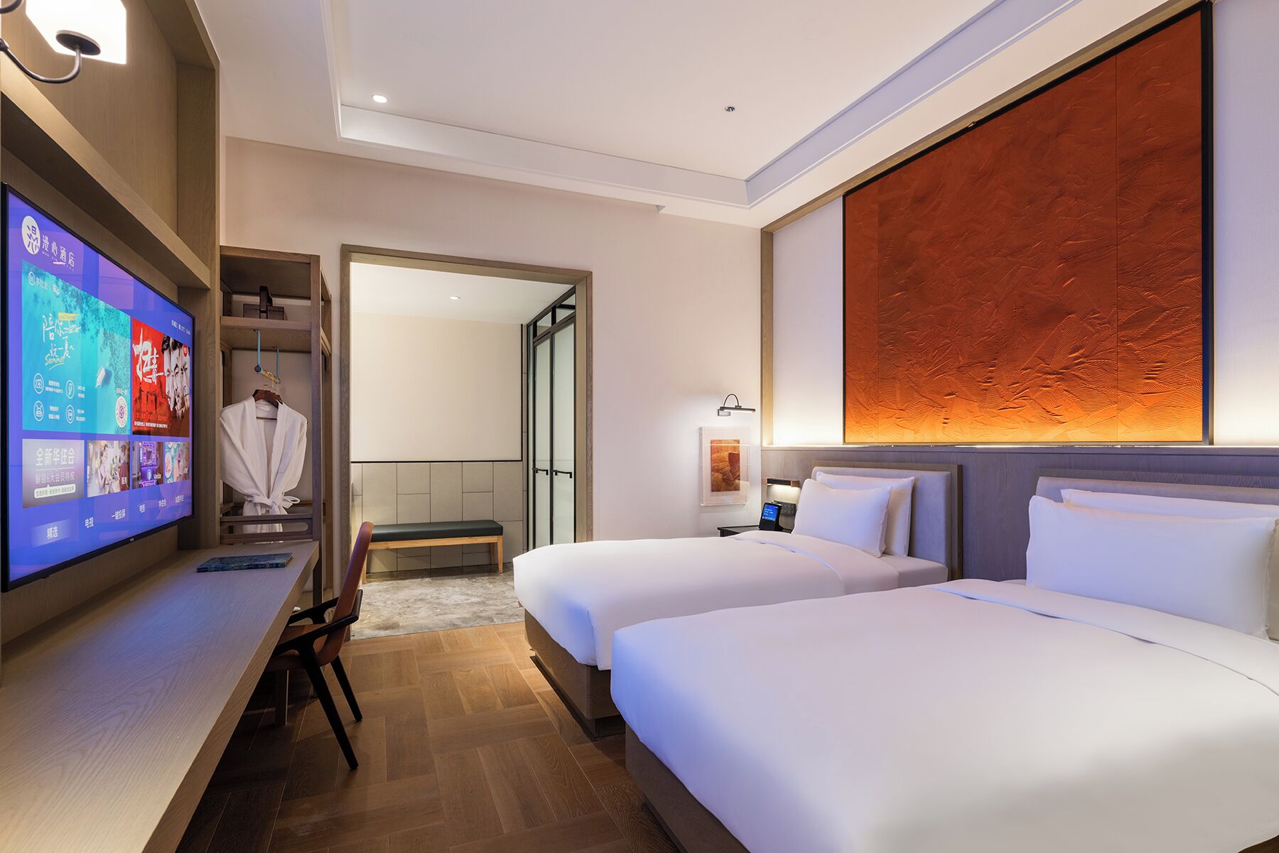 A hotel room with two beds, a TV, a desk, and a bathroom visible through an open door.