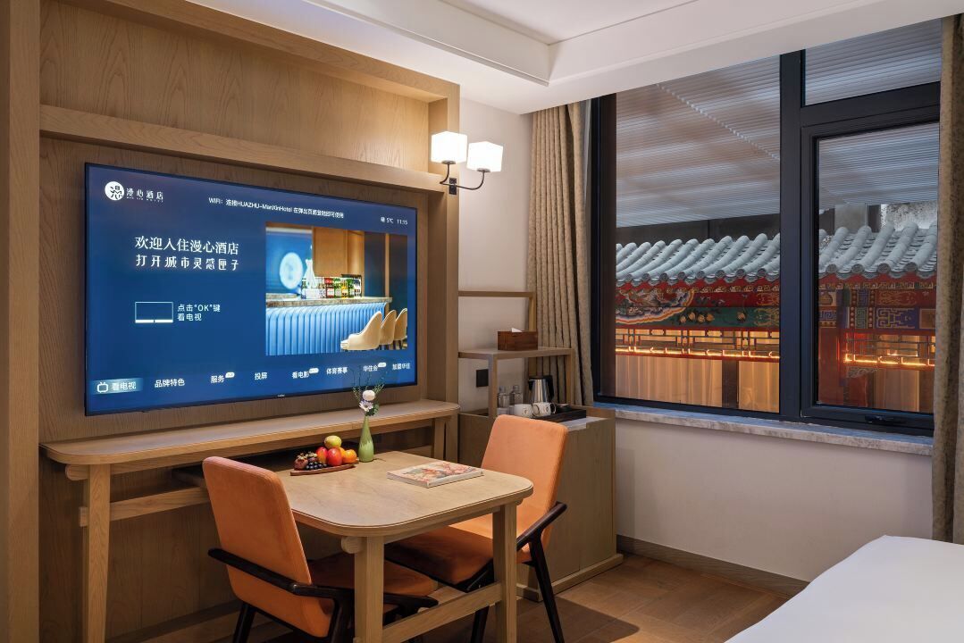 Habitación de hotel con una televisión mostrando un mensaje de bienvenida, un comedor con mesa y sillas, y una ventana con vista a la arquitectura china tradicional.