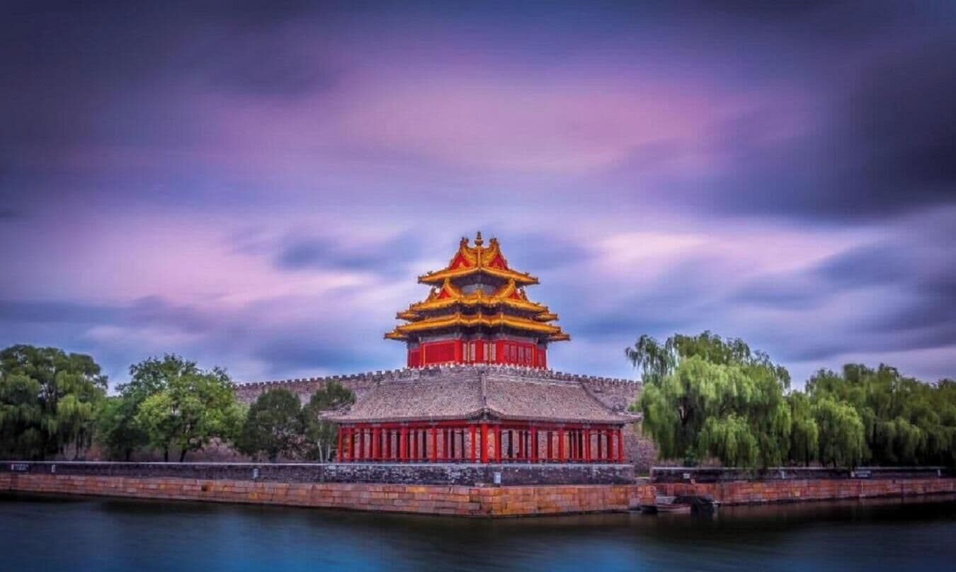 A traditional Chinese building with a red and yellow roof, surrounded by a body of water and trees.