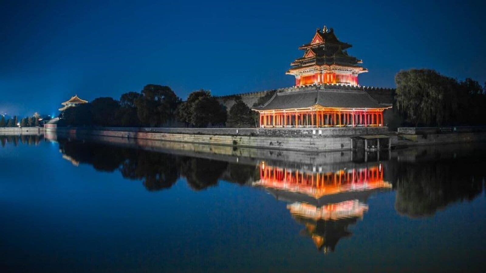 A traditional building with a reflection in calm water, surrounded by trees.