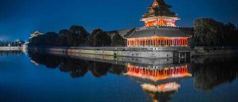 A traditional building with a reflection in calm water, surrounded by trees.
