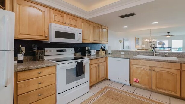 A modern kitchen with wooden cabinets, a microwave, a stove, and a sink. - Marks Beachfront Condo with 3rd Floor Balcony | Amazing Views + Pool (South Padre Island)