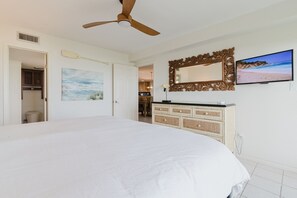 A bedroom with a large bed, a ceiling fan, a wooden dresser, a painting, and a TV on the wall. - Marks Beachfront Condo with 3rd Floor Balcony | Amazing Views + Pool (South Padre Island)