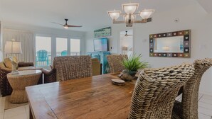 A dining area with a wooden table, wicker chairs, a ceiling fan, and a chandelier. - Marks Beachfront Condo with 3rd Floor Balcony | Amazing Views + Pool (South Padre Island)