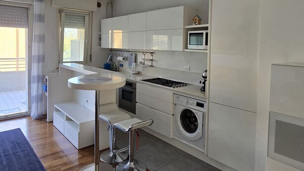 Uma cozinha compacta com forno embutido, micro-ondas e máquina de lavar roupa, uma pequena área de refeições e uma porta de vidro deslizante para o exterior.