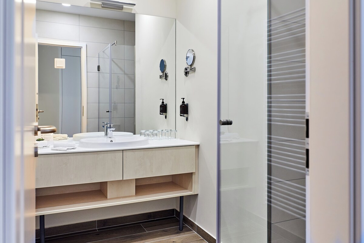 A modern bathroom with two sinks, a mirror, and a shower.