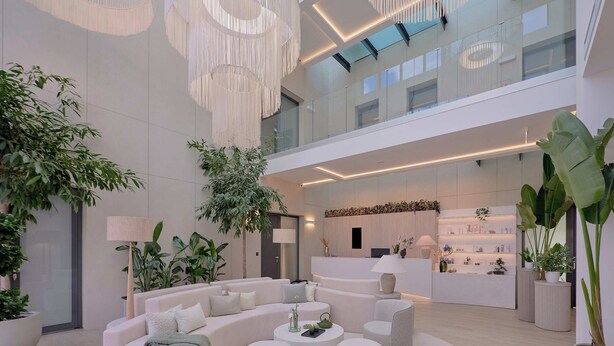 A spacious lobby with a modern white sofa, round ottomans, and potted plants. - Evergreen Health (Kehidakustány)