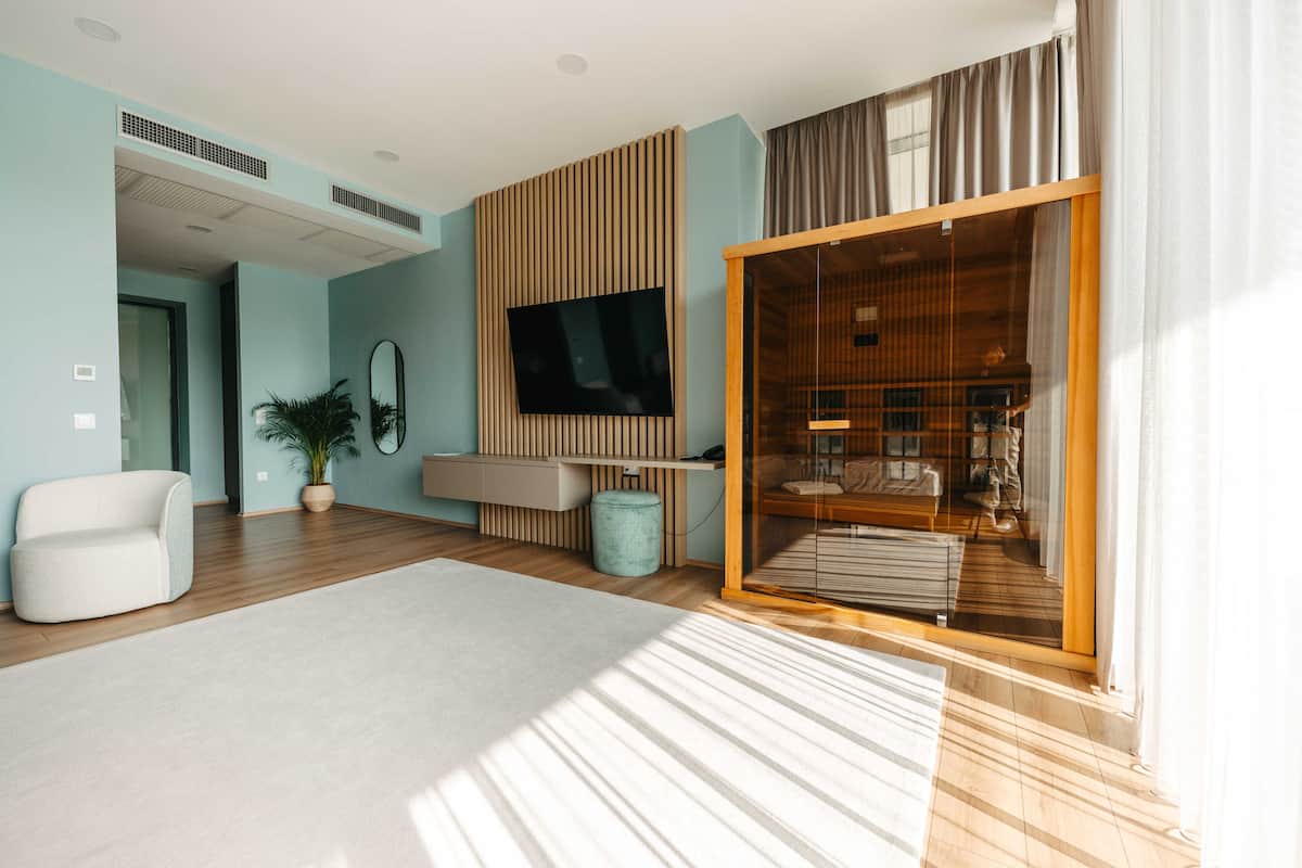 A modern living room with a flat-screen TV, a sofa, a potted plant, and a sliding glass door leading to a dining area.
