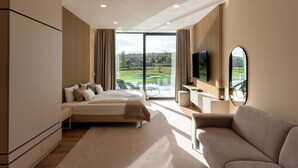 A modern hotel room with a large bed, a sofa, a TV, and a view of a golf course. - Evergreen Health (Kehidakustány)