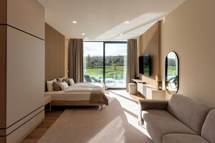Una habitación de hotel moderna con una cama grande, un sofá, un televisor y vistas a un campo de golf.