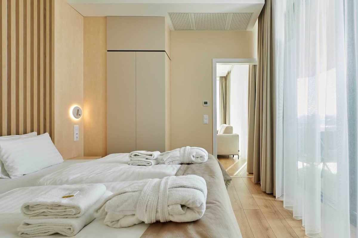 A hotel room with a bed, towels, a nightstand, a wall clock, and a window with curtains.
