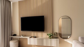 A modern living room with a flat-screen TV mounted on a wooden panel wall, a round mirror, a sofa, and a small ottoman. - Evergreen Health (Kehidakustány)