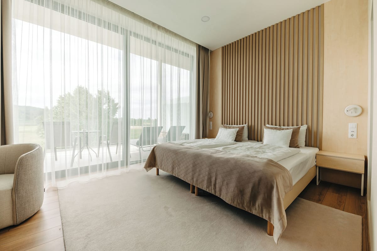 A modern bedroom with a large bed, a chair, and a view of the outdoors.