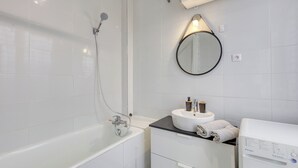 Ein modernes Badezimmer mit einer Badewanne, einem runden Spiegel, einem Waschbecken mit Handtuch und einer Waschmaschine.