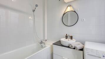 A modern bathroom with a bathtub, a round mirror, a sink with a towel, and a washing machine.