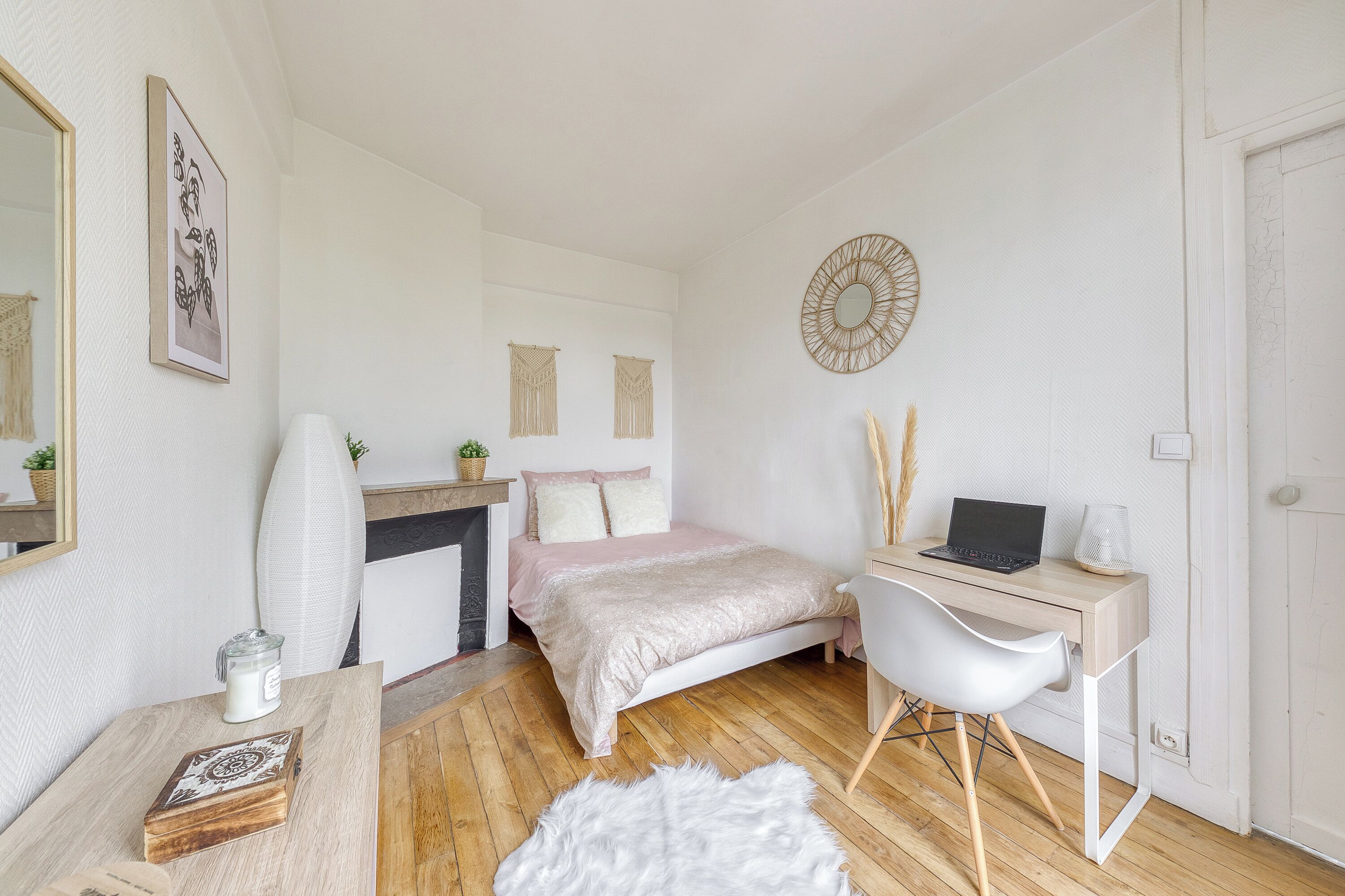 A bedroom with a bed, a desk, a chair, a mirror, and a fireplace.