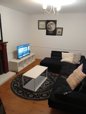A living room with a TV on a white stand, a black sofa with patterned cushions, a white coffee table, and a black and white patterned rug. - The Linwood Terrace (Eastwood)