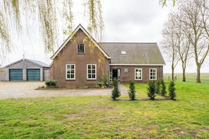 A two-story brick house with a gabled roof, a garage, and a small front yard with young trees.