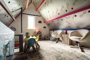 A room with a sloped ceiling, a table with chairs, a window, and a play area with toys.
