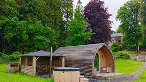 A rustic wooden cabin with a sloped roof, a small porch, and a hot tub. - Accessibile Craigengillan Cabin (Dalmellington)