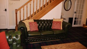 A living room with a green leather sofa, a plaid rug, a wooden coffee table, a wooden staircase, and a mirror on the wall. - Find Me Out - Craigengillan Estate (Dalmellington)