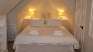 A bedroom with a sloped ceiling, two bedside lamps, a framed picture on the wall, and neatly folded towels on the bed. - Find Me Out - Craigengillan Estate (Dalmellington)