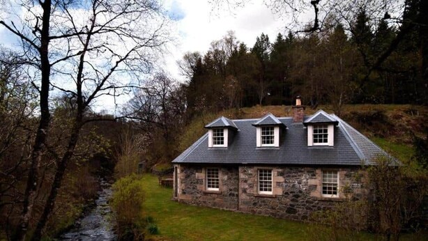 A stone house with a gabled roof, a small stream in front, and a wooded hillside. - Find Me Out - Craigengillan Estate (Dalmellington)